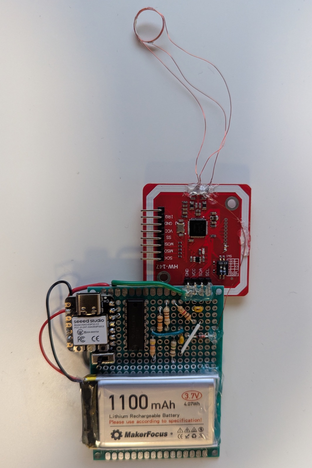 Front of the wearable: a XIAO ESP32-C3, a PN532 NFC reader, an envelope-detector circuit on protoboard, and a 1100mAh battery, with a hand-wound antenna coil on a thin lead