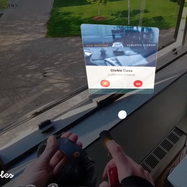 View through Snap Spectacles: a translucent Spotify player overlay floats above a pair of headphones held in both hands, showing a Ludovico Einaudi track