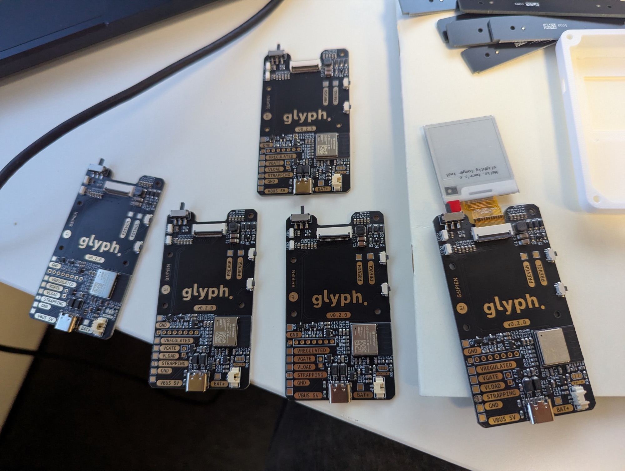 Several manufactured Glyph v2 boards laid out, with an early e-ink display test